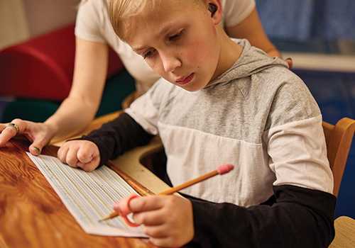 A boy practices writing with an adapted pencil grip on a slant board as a part of his occupational therapy.