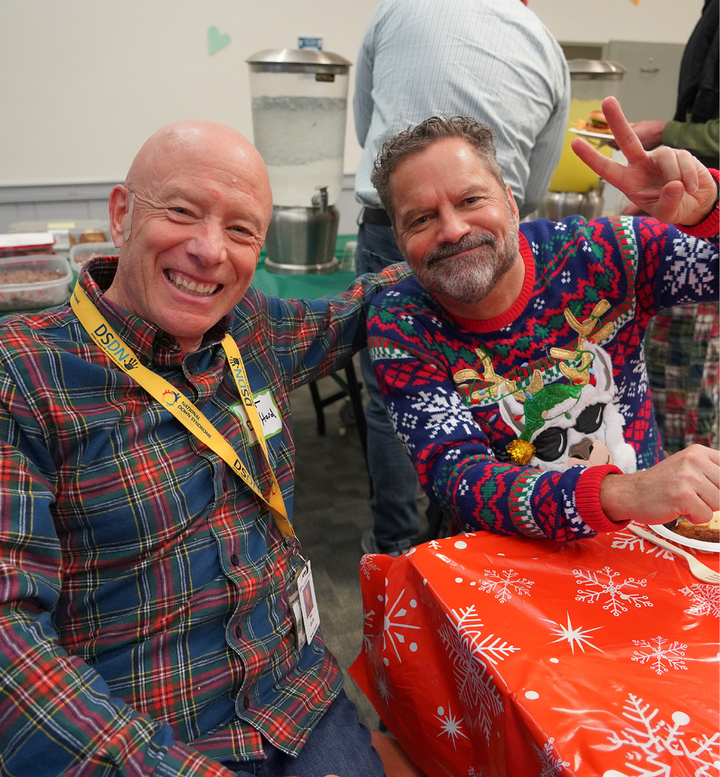 Two older men sitting together enjoying a festive holiday party at work.