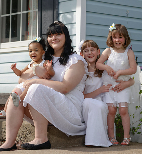 A young woman holds her daughter in her arms as they sit with family