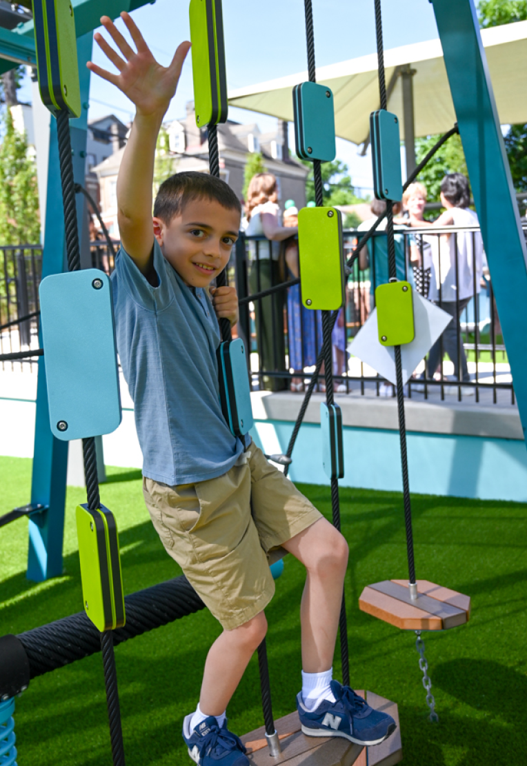 A young boy with his arm raised up is playing on a colorful blue and green jungle gym